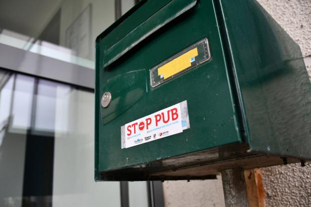 Gros plan sur une boîte aux lettre verte avec un autocollant Stop Pub